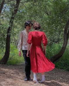 two people dressed in red are walking through the woods with their backs to each other