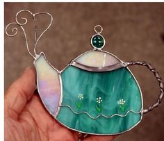 a hand holding a stained glass teapot ornament