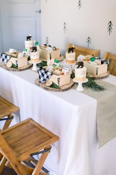 a table topped with lots of cakes on top of wooden chairs next to a white table cloth