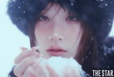 a young woman is blowing snow with her hands in front of her face and wearing a black hat