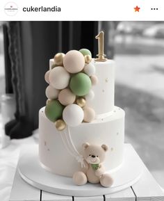 a white cake with balloons and a teddy bear on the bottom tier is sitting on a table