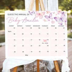 a baby shower calendar on an easel with pink butterflies and white ruffles