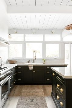 a large kitchen with black cabinets and white counter tops, an area rug on the floor