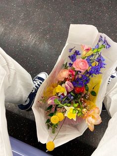 a person holding a bouquet of flowers on top of a blue bench with white pants