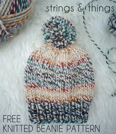 a knitted beanie hat sitting on top of a white fur rug next to yarn