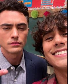 two young men posing for the camera in front of a chalkboard