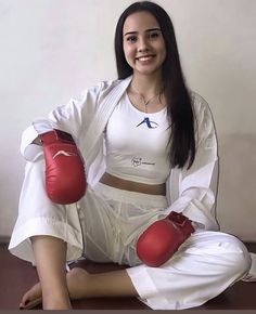 a woman sitting on the floor wearing red boxing gloves and white shirt with her arms crossed