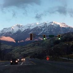 cars are driving down the road in front of snow covered mountain tops and traffic lights