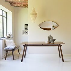 a wooden table sitting in front of a window next to a chair and mirror on the wall