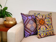 a couch with two pillows on it next to a potted plant and a gold vase