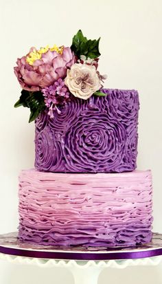 a three layer cake with purple icing and flowers on top