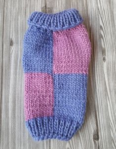 a blue and pink knitted dog sweater laying on top of a wooden floor