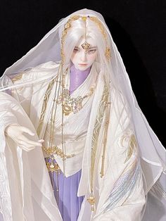 a doll dressed in white and gold with a veil on her head, wearing a purple dress