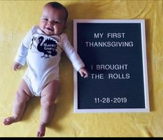 a baby laying next to a sign that says, my first thanksgiving i brought the rolls