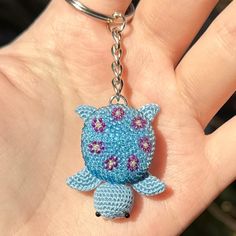 a hand holding a small blue turtle keychain on it's thumb,