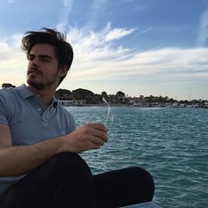 a man sitting on the edge of a boat holding something in one hand and looking off into the distance