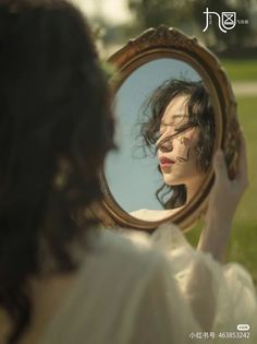 a woman is looking at her reflection in the mirror while she's holding it up