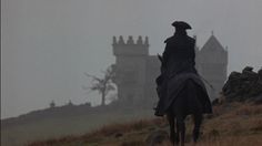 a man riding on the back of a horse in front of a castle covered in fog