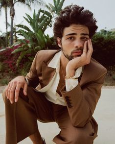 a man in a brown suit and white shirt is leaning on his hand to his face