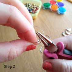 a person is holding a pair of scissors in their hand with beads on the table behind them