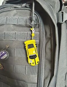 a yellow toy car is attached to the back of a gray backpack with keychain