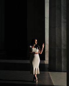 a woman in a white dress is walking through an empty room with columns on either side