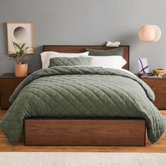 a bed with green comforter and pillows on top of it in a bedroom next to a wooden dresser