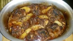 a pot filled with meat and potatoes on top of a wooden table next to a stove