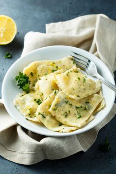 a white bowl filled with ravioli on top of a blue surface next to a lemon slice