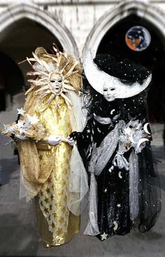 two dolls dressed in black and gold standing next to each other on the sidewalk near an archway