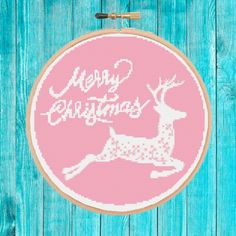 a cross stitch christmas ornament hanging on a blue wooden background with the words merry christmas