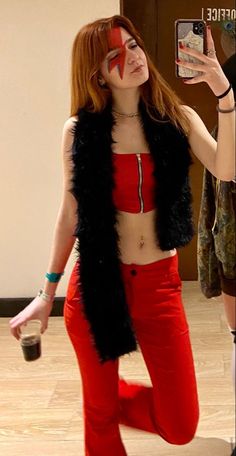 a woman in red pants and black vest taking a selfie with her cell phone