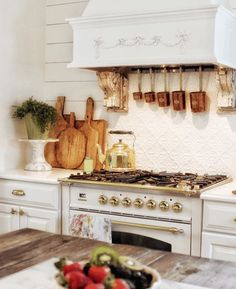 a bowl of fruit is sitting on the table in front of an oven with utensils hanging above it