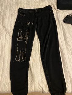 a pair of black jeans with an image of a cat drawn on them are laying on a bed