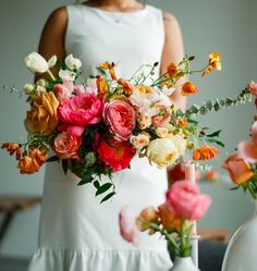 a woman holding a bouquet of flowers in front of two vases