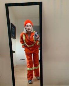 a woman in an orange jumpsuit is taking a selfie with her cell phone