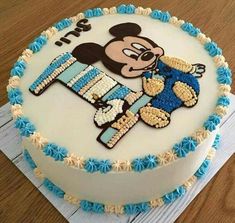 a mickey mouse cake with blue and white frosting on it's side, sitting on a wooden table