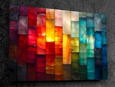 a multicolored wall hanging on the side of a cement wall with an orange light shining through it