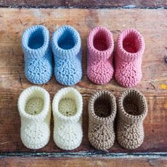 four crocheted baby shoes lined up on a wooden surface