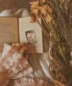 an open book sitting on top of a bed next to flowers