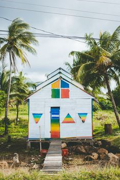 a white house with rainbow painted on the side and steps leading up to it, surrounded by palm trees