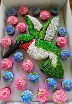 a cake in the shape of a hummingbird surrounded by cupcakes and flowers