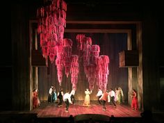 a group of people standing on top of a stage under pink chandelier hanging from the ceiling