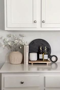 a white dresser with some bottles and candles on it's shelf next to a vase filled with flowers