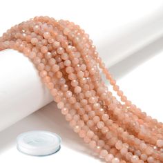 several strands of light pink beads on a white surface next to a tube of toothpaste