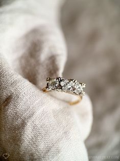 a three stone diamond ring sitting on top of a white cloth covered bedding area