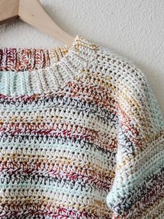 a crocheted sweater hanging on a wooden hanger next to a white wall