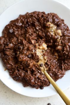 a white plate topped with chocolate oatmeal next to a wooden spoon on top of a table