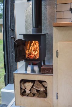 a small stove with wood in it next to a wall mounted oven and door open