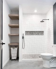 a white toilet sitting in a bathroom next to a walk in shower and wooden shelves